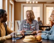 Happy residents dining together in a community setting, demonstrating the engaging lifestyle and pros of senior living communities.